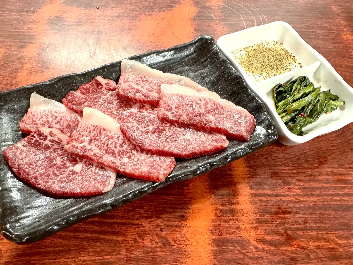 熟成塩カルビ。黒い皿に盛り、スパイス塩とニラ醤油を添えて