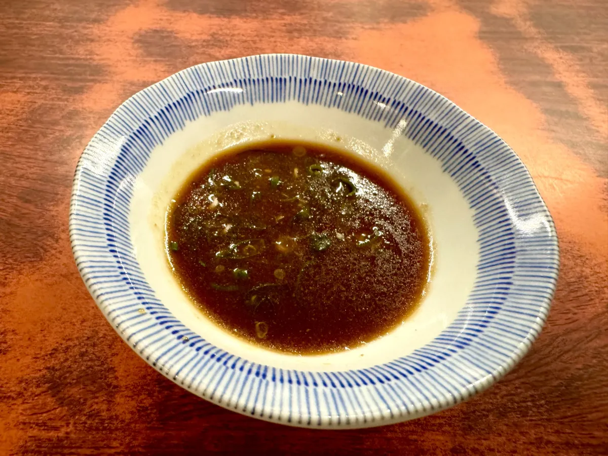青い十草柄の小皿に入れた、刻みねぎ入りの創業以来の秘伝のタレ